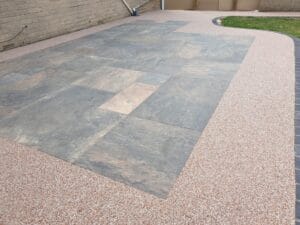 A paved courtyard with large, textured stone tiles in the center, surrounded by small pebbled concrete. Grass borders one side, creating an orderly, calm scene