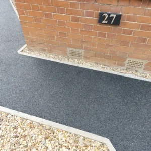 Gray stone steps with dark blue side walls lead to a modern gray door. Green grass surrounds, with a blue pot on the right, creating a clean, inviting entrance